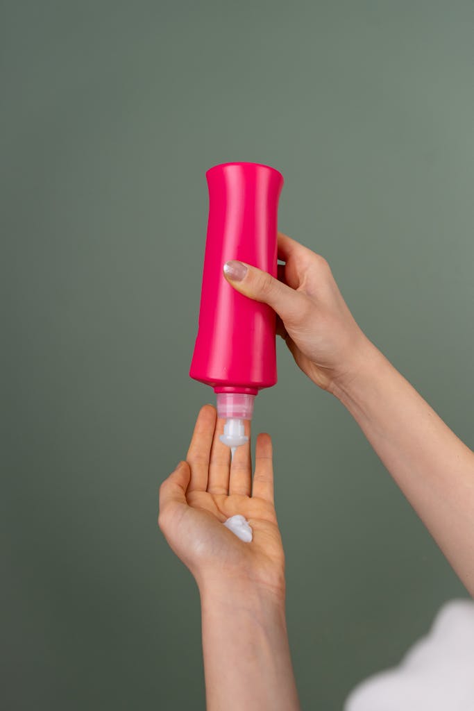 Hand applying cream from a bright pink bottle, skincare routine concept.